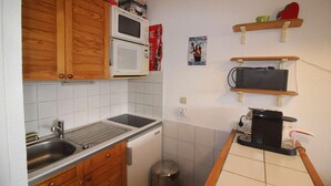 Une cuisine compacte avec des meubles de rangement en bois, un four à micro-ondes, un évier et une petite poubelle.