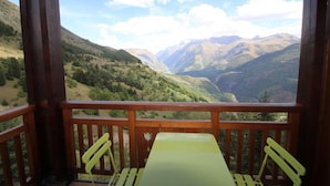 Une terrasse en bois avec une table et des chaises, offrant une vue sur un paysage montagneux.