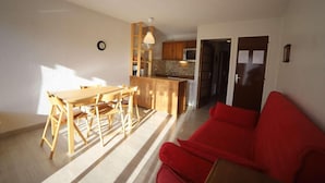 Un espace de vie compact comprenant un coin repas, une kitchenette et un canapé rouge.