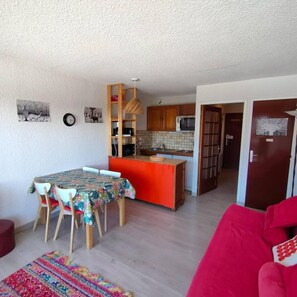 A compact living space with a dining area, kitchen, and a red sofa. - Resort center, 2nd floor, view open, balcony, tv, 27m², Auris en Oisans (Auris)