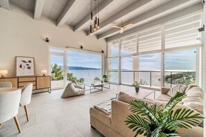 A spacious living room with a large window overlooking a scenic view, a cozy seating area, and a minimalist design. - Villa Vid - Five Bedroom Villa, Sleeps 10 (Vela Farska)