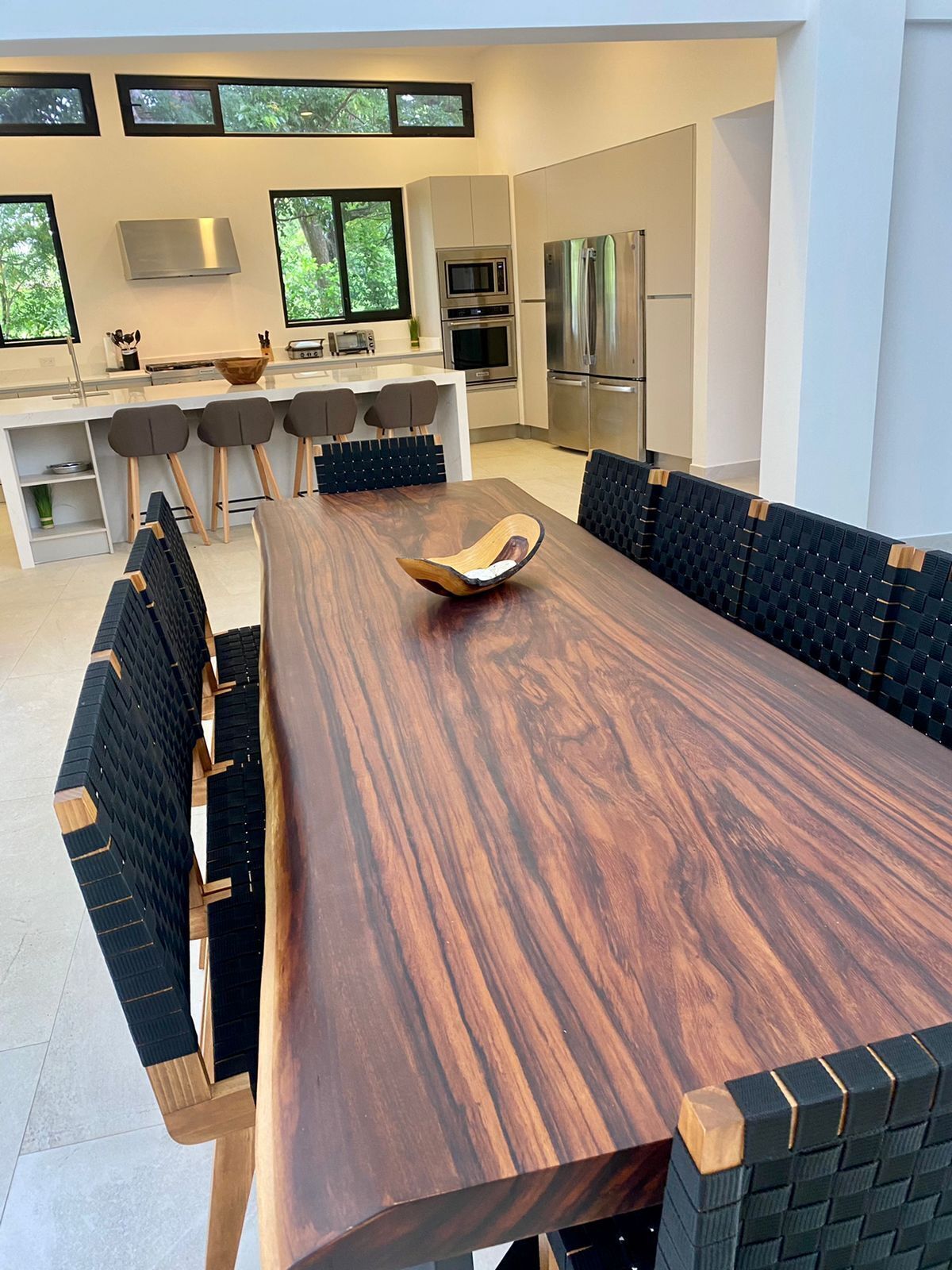 Une cuisine moderne dotée d’un îlot central, d’appareils électroménagers intégrés et d’un coin repas avec une longue table en bois et des bancs recouverts de tissu noir.