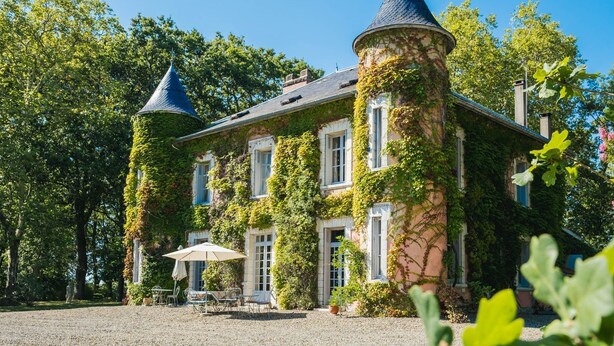 Ein Schloss mit zwei Türmen, einer mit Efeu bewachsenen Mauer und einem Kieshof mit Außenbestuhlung.