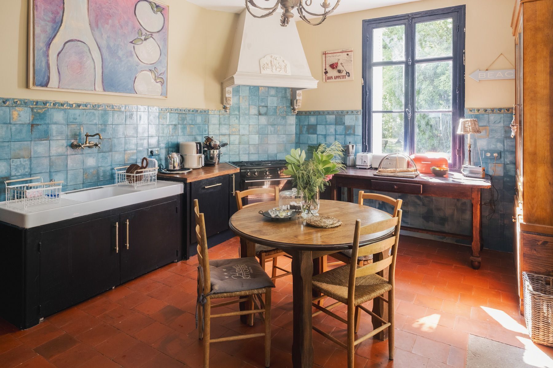Une cuisine avec une table ronde en bois, des meubles de rangement sombres et un dosseret de carrelage bleu.