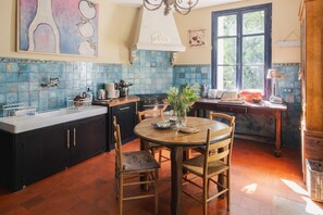 A kitchen with a round wooden table, dark cabinets, and blue tiled backsplash. - Chateau Bellevue - Eight Bedroom Castle, Sleeps 16 (Sainte-Marie-de-Gosse)