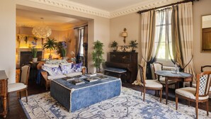 A living room with a blue ottoman, a fireplace, a piano, and a dining area.