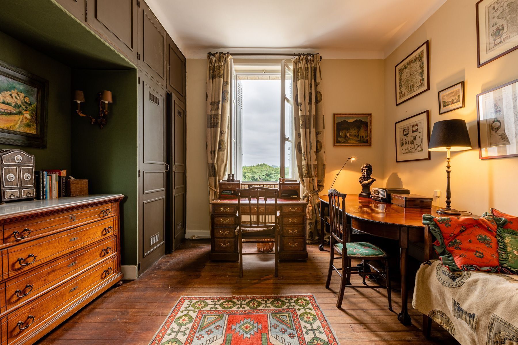 Une chambre traditionnelle avec un bureau en bois, une chaise, un lit recouvert d’une couverture à motifs et une commode à tiroirs.