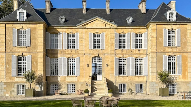 A large, historic building with symmetrical architecture, multiple windows with shutters, and a central entrance with steps leading up to it.