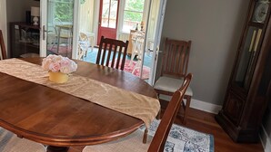 Un comedor con una mesa de madera, sillas, un jarrón de flores y un reloj de pie grande.