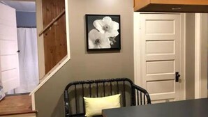 Una habitación con una silla de mimbre negro, una puerta blanca y un cuadro en la pared.