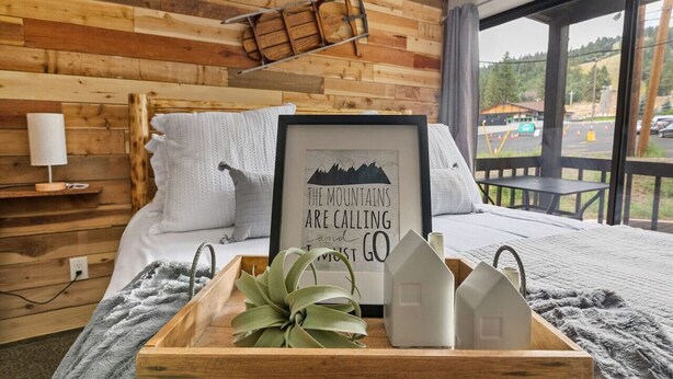 A cozy bedroom with a wooden headboard, a framed inspirational quote, a bedside table with a lamp, and a view of the outdoors. - Pet Friendly + Ski In Out Unobstructed Views (Big Bear Lake)