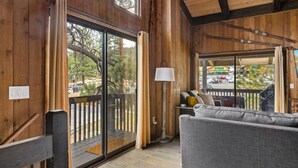 A wooden interior with a sliding glass door leading to a balcony, a grey sofa, and a floor lamp. - Pet Friendly + Ski In Out Unobstructed Views (Big Bear Lake)