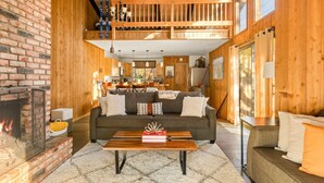 A cozy cabin interior with a fireplace, a dining area, and a loft space. - Pet Friendly + Ski In Out Unobstructed Views (Big Bear Lake)