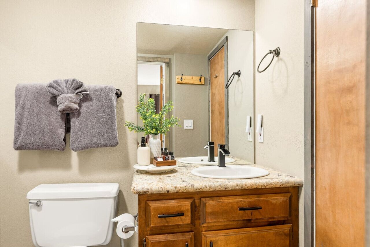 Een badkamer met toilet, wastafel, houten wastafelmeubel en een spiegel.