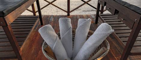 A beachside wooden deck with a woven basket holding white towels, overlooking the ocean.