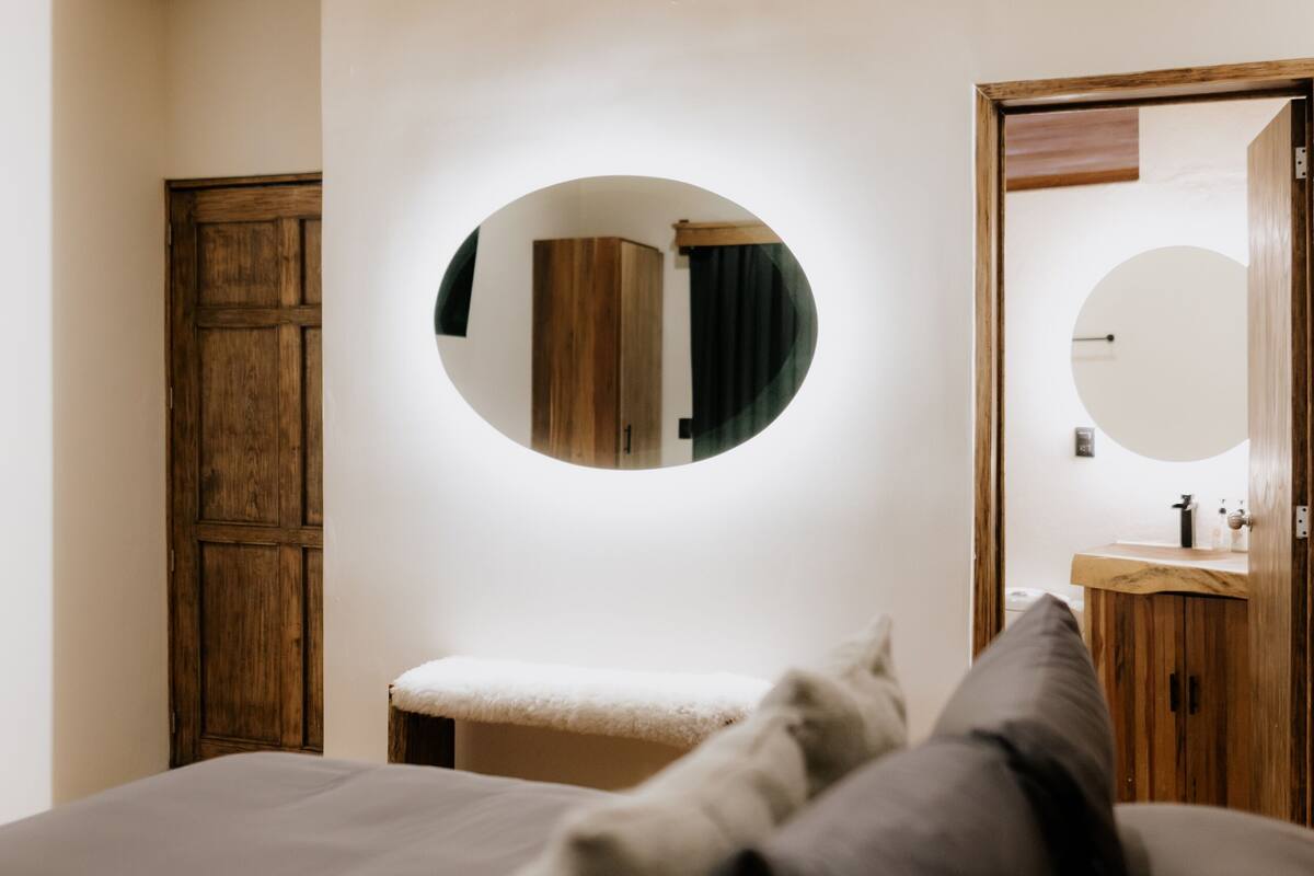 Un dormitorio con techo de madera, un espejo redondo, un armario de madera y una cama con almohadas.