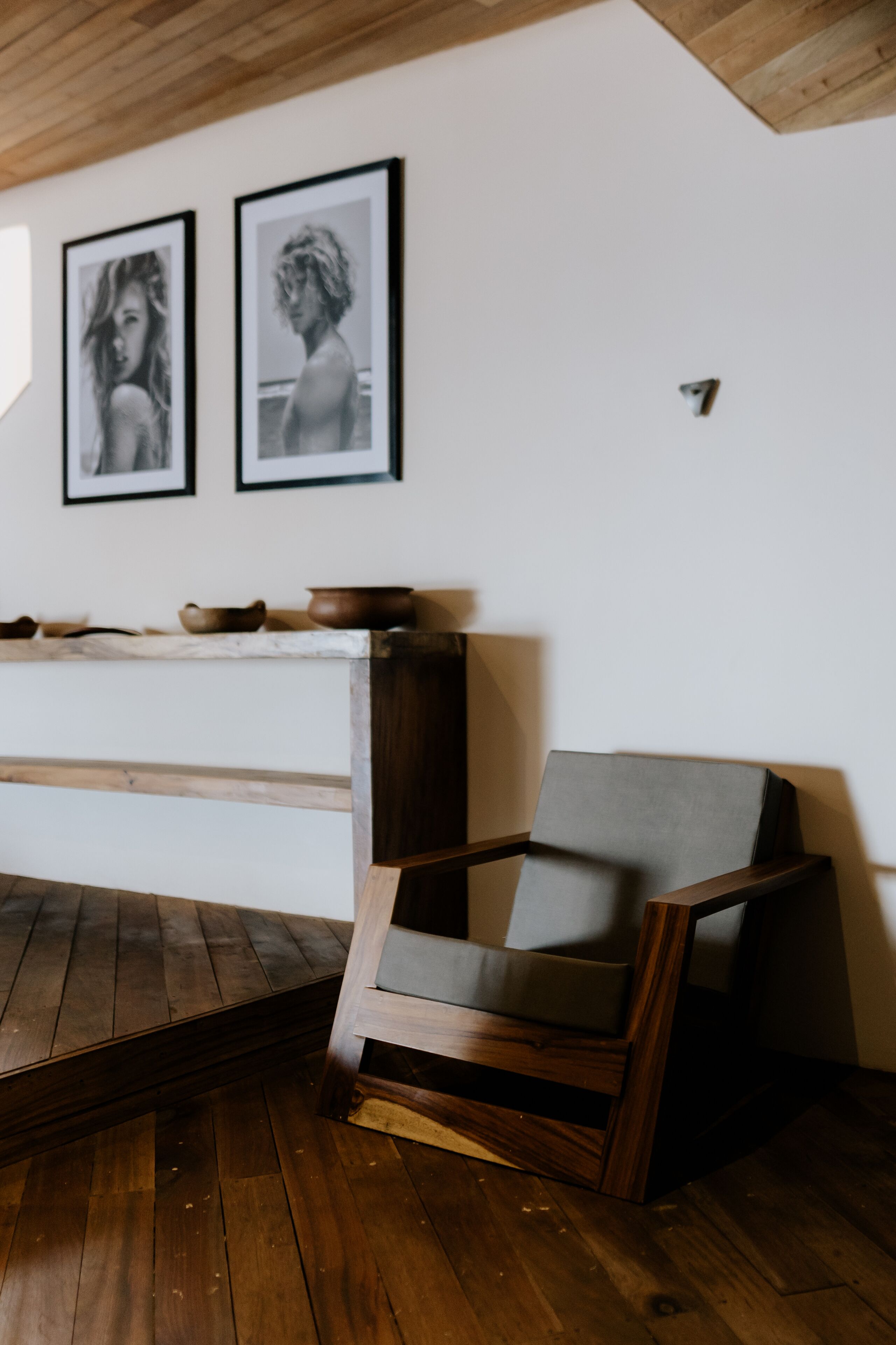 A room with wooden flooring, a wooden bench, a chair, and two framed pictures on the wall.