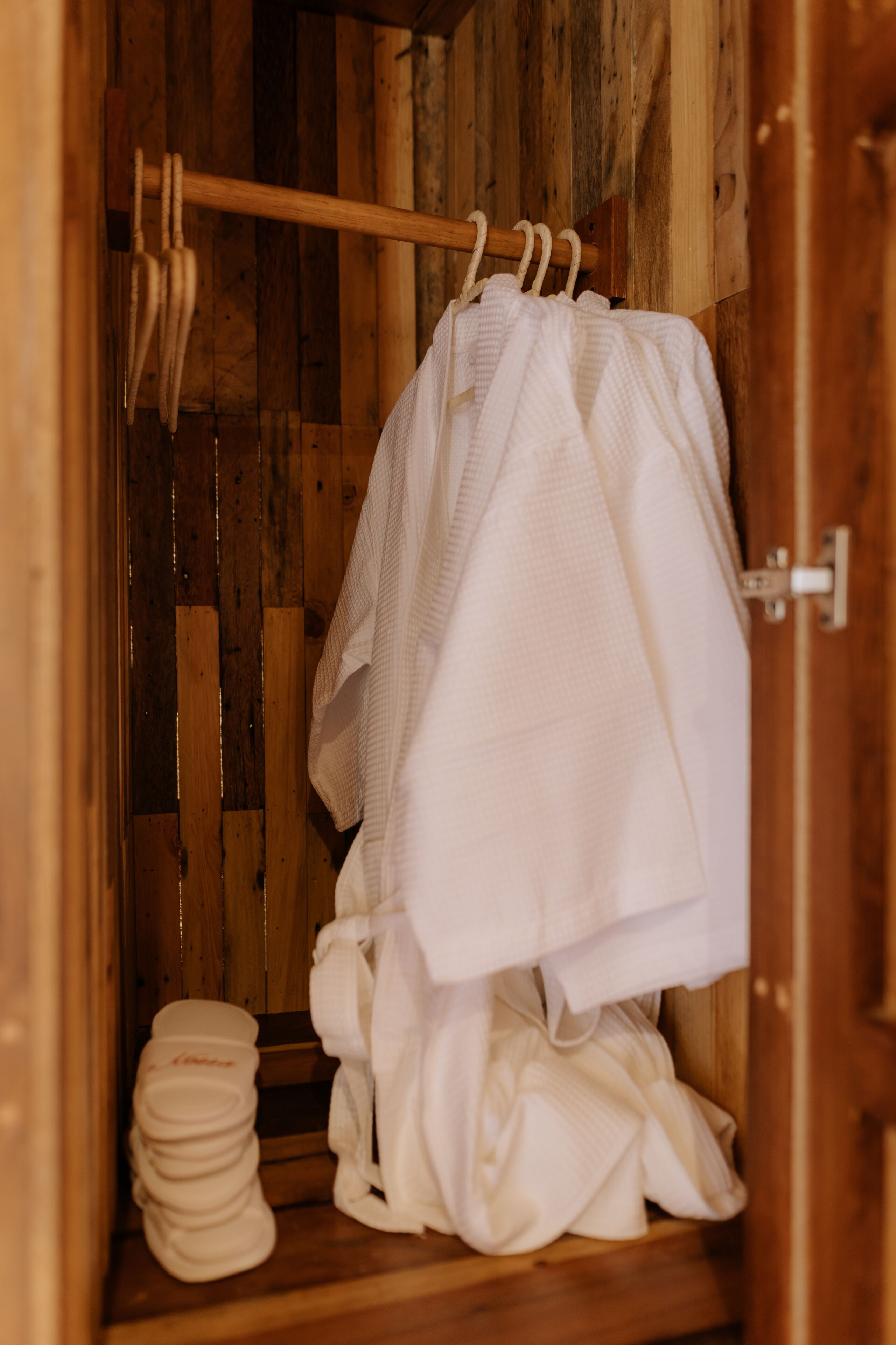 A wooden cabin interior with a wooden bench, a wooden door, and a rack holding white towels.