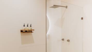 Un espace douche clos par des parois de verre, avec un plafond en bois, une petite étagère contenant des articles de toilette et un sol à motifs.