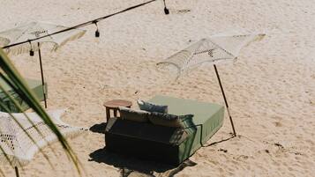 Una playa con una única silla de descanso verde, una pequeña mesa, luces colgantes y un paraguas de playa.