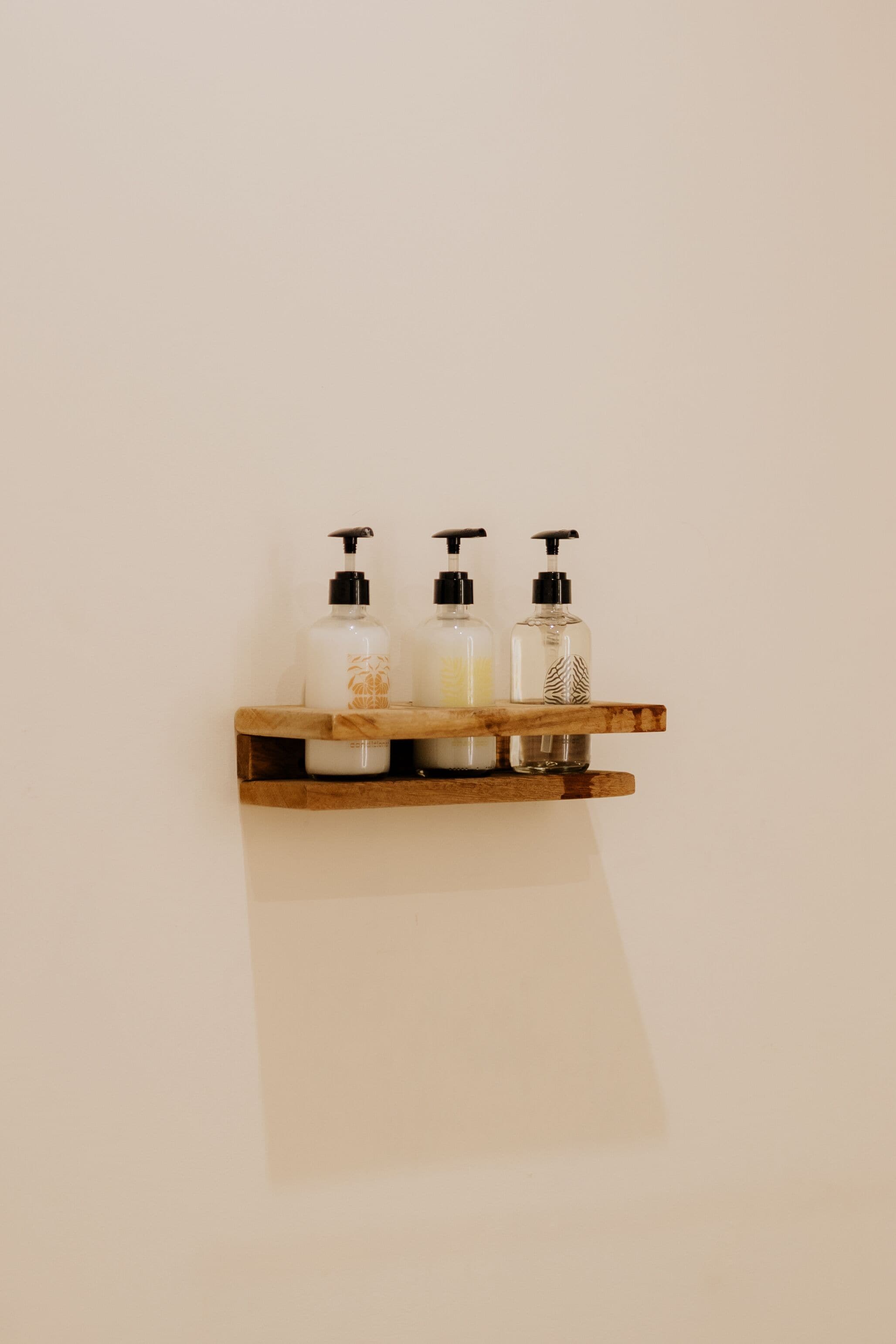Une étagère en bois sur laquelle sont posées trois bouteilles en verre contenant des produits de toilette.