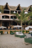 Un hotel frente a la playa con varios niveles, techos de paja y zonas de estar al aire libre con sombrillas.