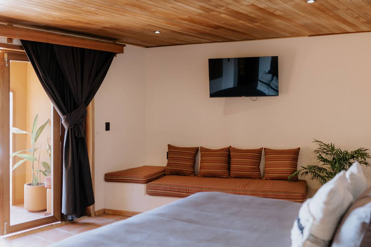 Un dormitorio con una cama grande, techo de madera, un televisor de pantalla plana en la pared y una planta en maceta.