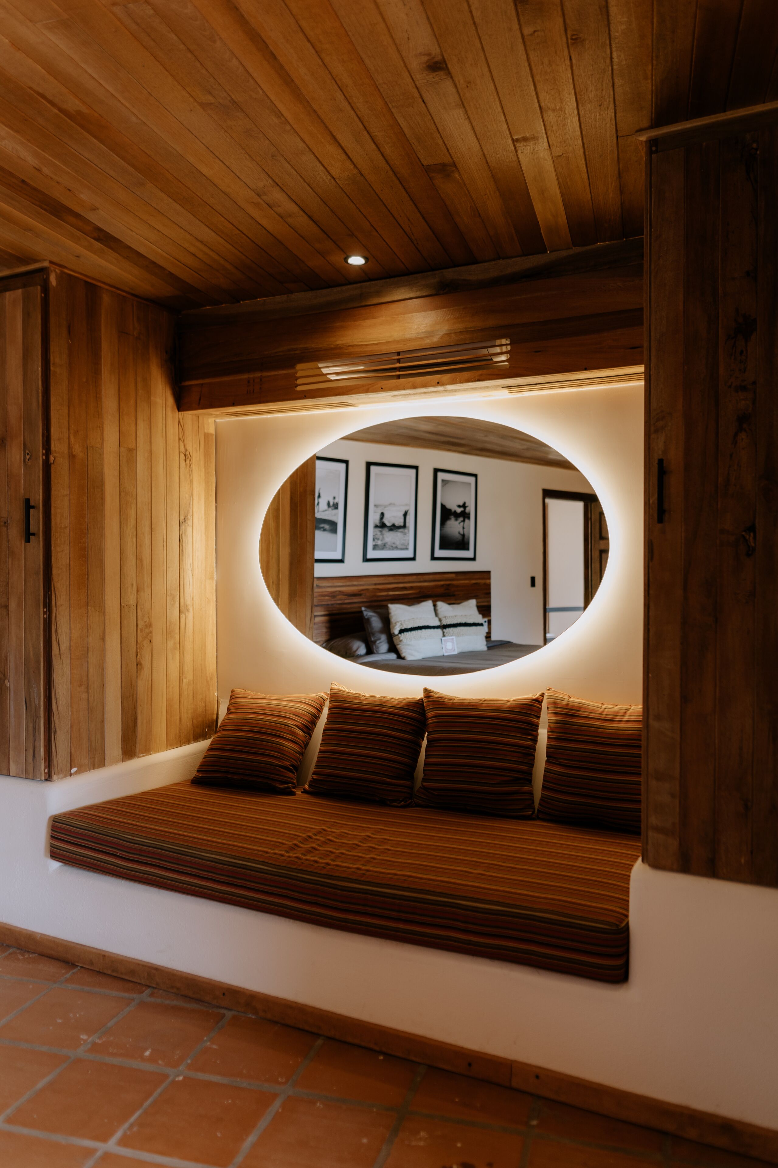 A cozy wooden bench with cushions, a circular mirror, and framed pictures on the wall.