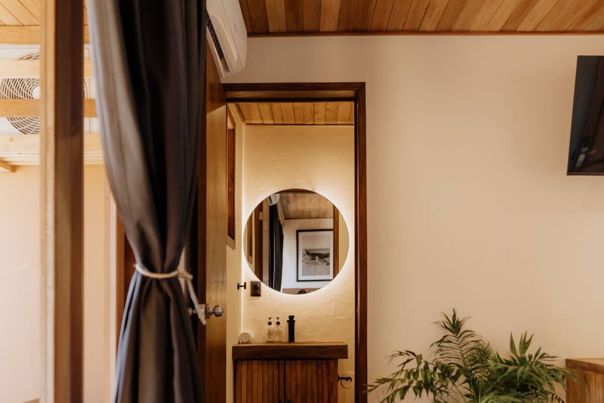 Una habitación con techo de madera, un espejo, un lavabo, una planta y una cama.