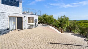 Una casa moderna con entrada pavimentada, un balcón de cristal y vista al mar.