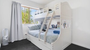 Habitación con literas, ventana, cortinas, radiador y estantería.