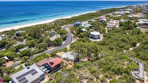 Vista aérea de una zona residencial costera con casas, una playa y un cielo azul despejado.