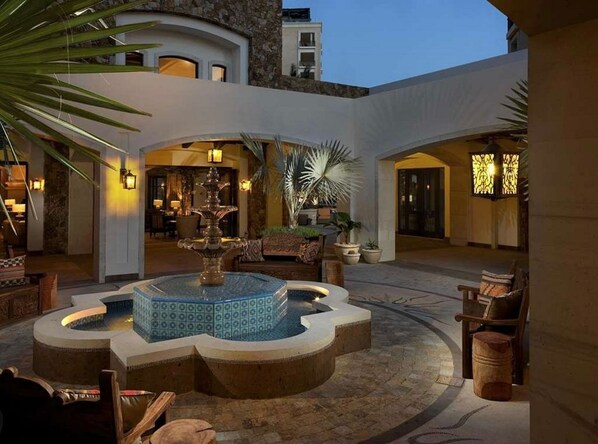 A courtyard with a central fountain, seating areas, and a pool.