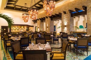 A restaurant with multiple dining tables and chairs, a kitchen area, and decorative lighting. - LUXURY STUDIO 5🎖️ LOS CABOS, SAN LUCAS, MEXICO (Cabo San Lucas)