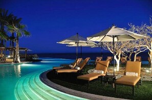 A poolside area with lounge chairs and umbrellas, overlooking a body of water at night.