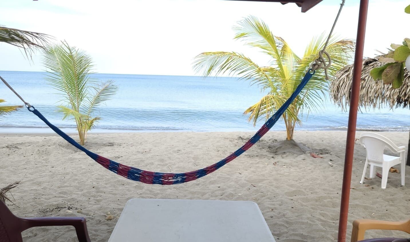 A hammock on a beach with a view of the ocean, a white table, and a few chairs.