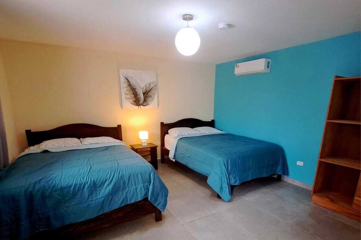 Une chambre avec deux lits, un luminaire au plafond, un climatiseur et une étagère en bois.