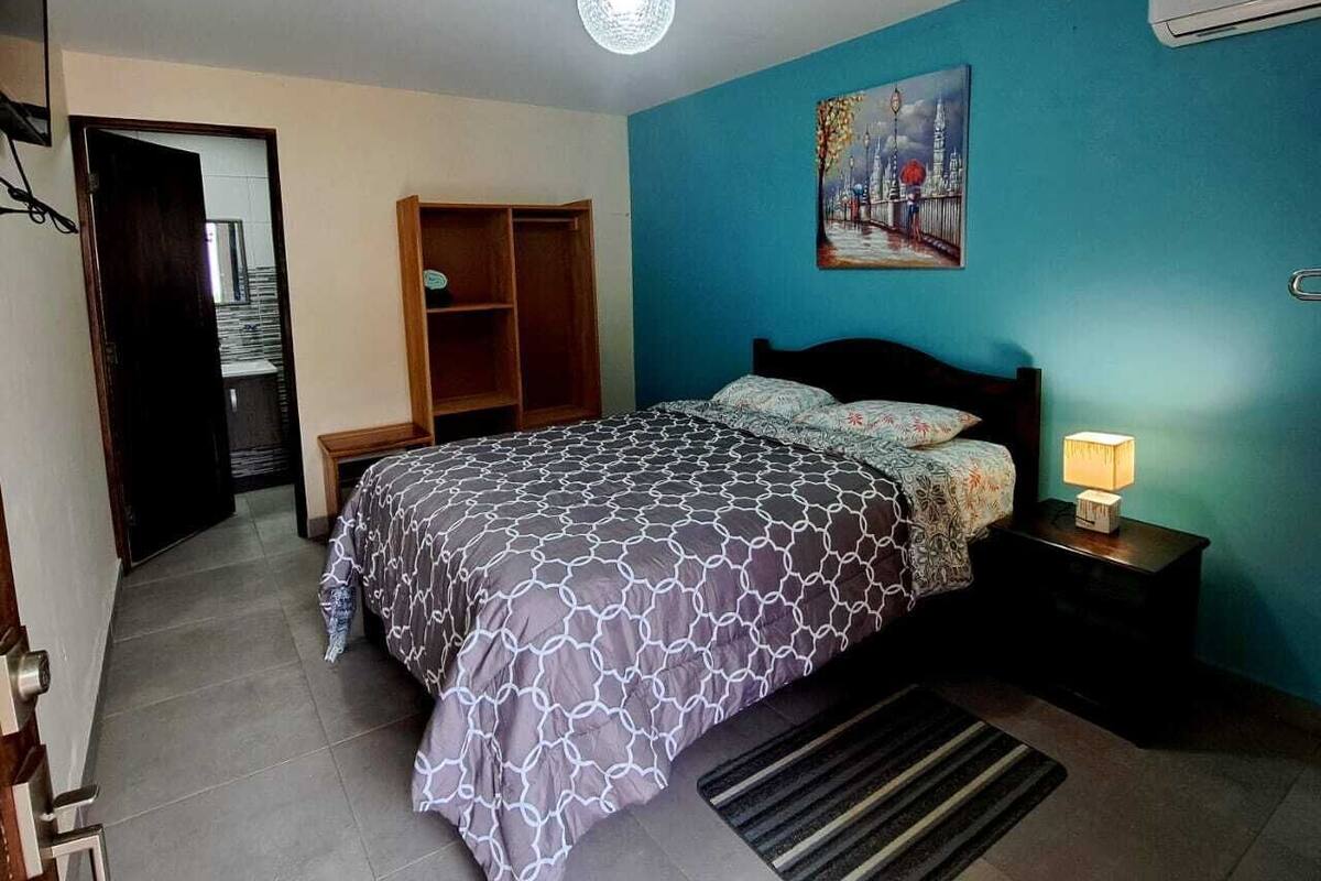 Une chambre à coucher avec un lit, une table de chevet avec une lampe, une armoire et un tableau au mur.