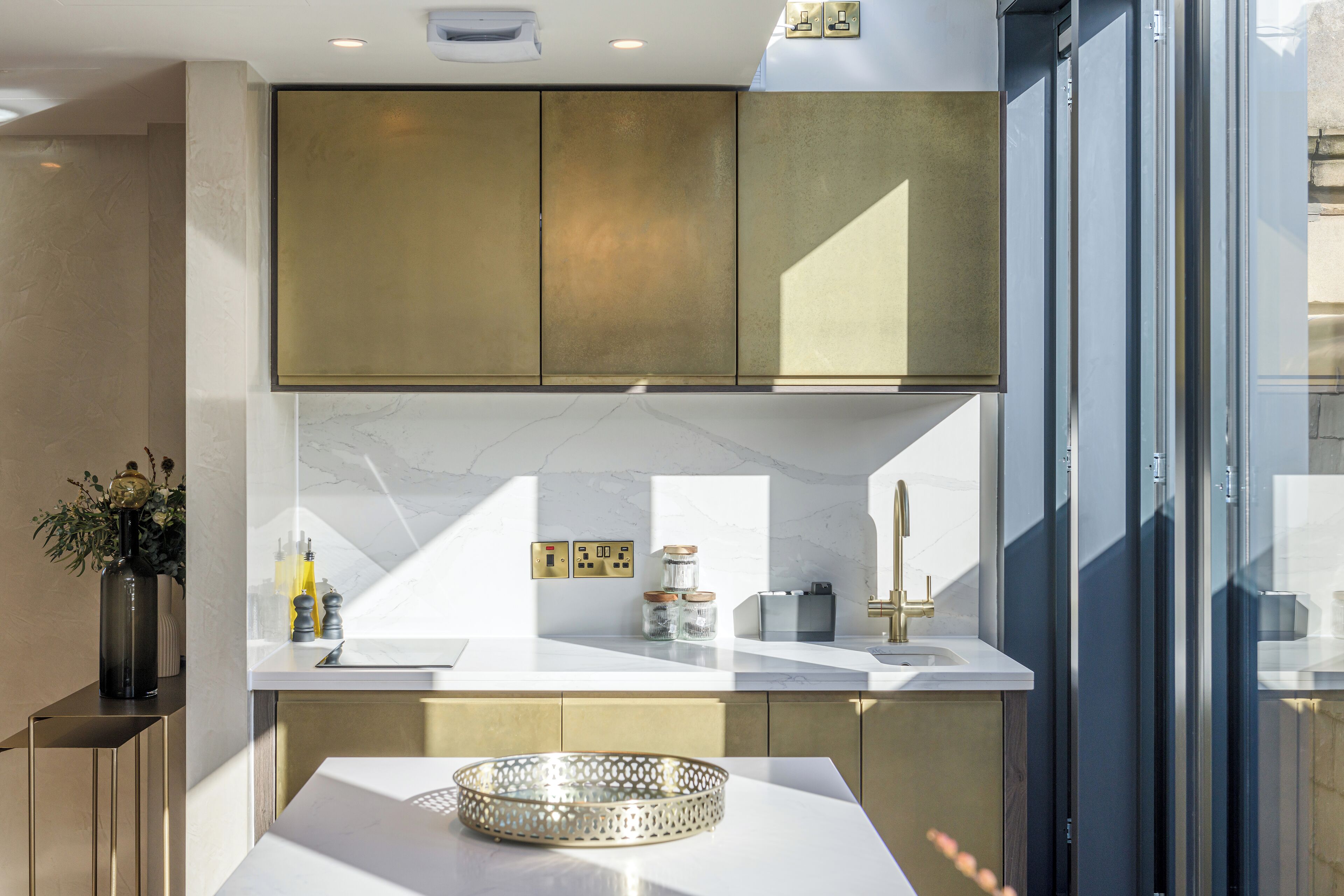 Una cucina moderna con un piano di lavoro bianco, mobili dorati e un'ampia finestra.