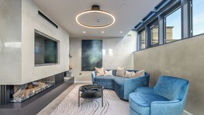 Een moderne woonkamer met een open haard, blauw meubilair en een groot raam.
