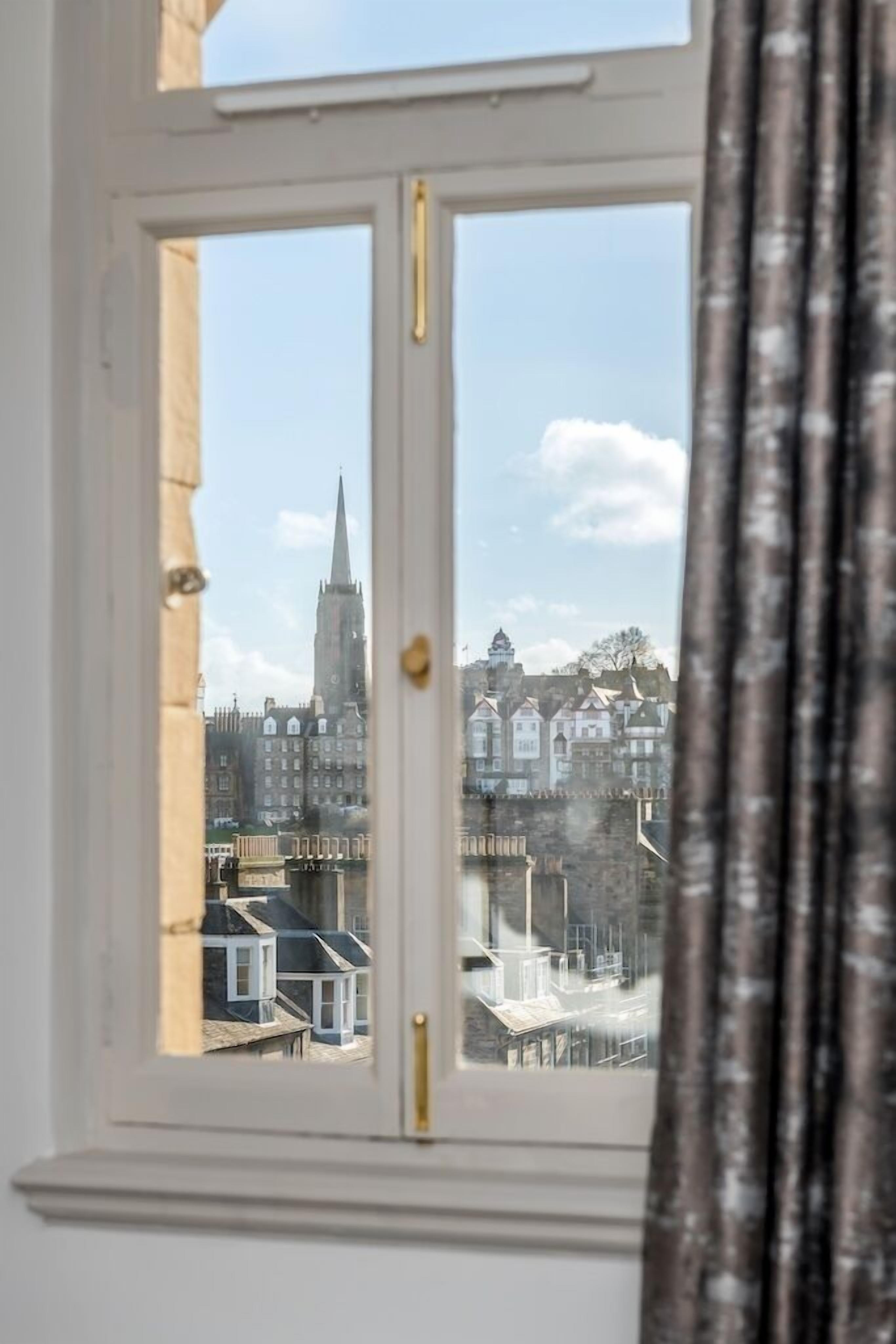 Ein Fenster mit Blick auf eine Stadtlandschaft, darunter ein markanter Kirchturm und Wohnhäuser.