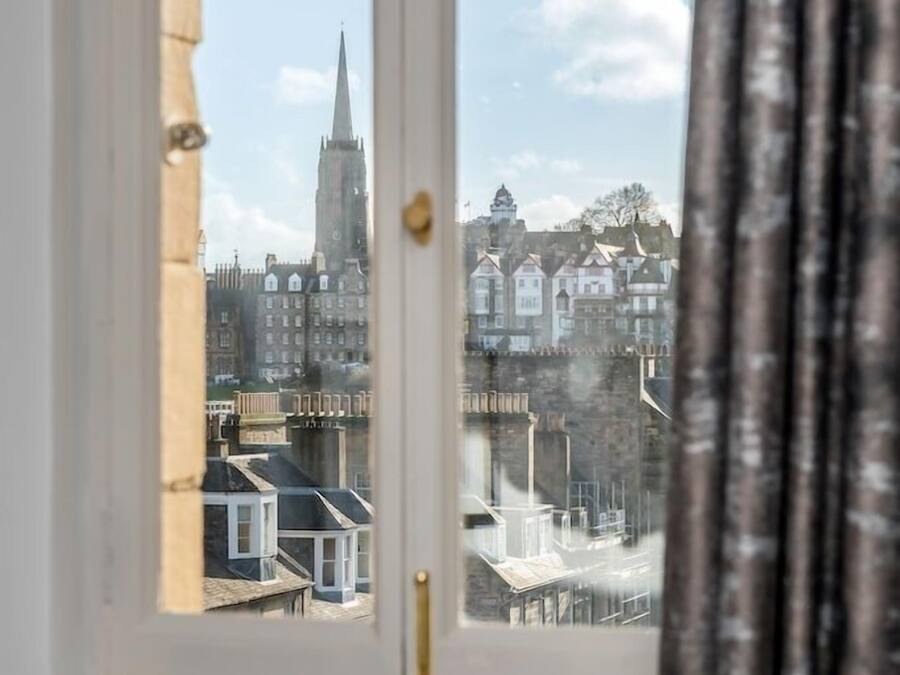 Ein Fenster mit Blick auf eine Stadtlandschaft, darunter ein markanter Kirchturm und Wohnhäuser.