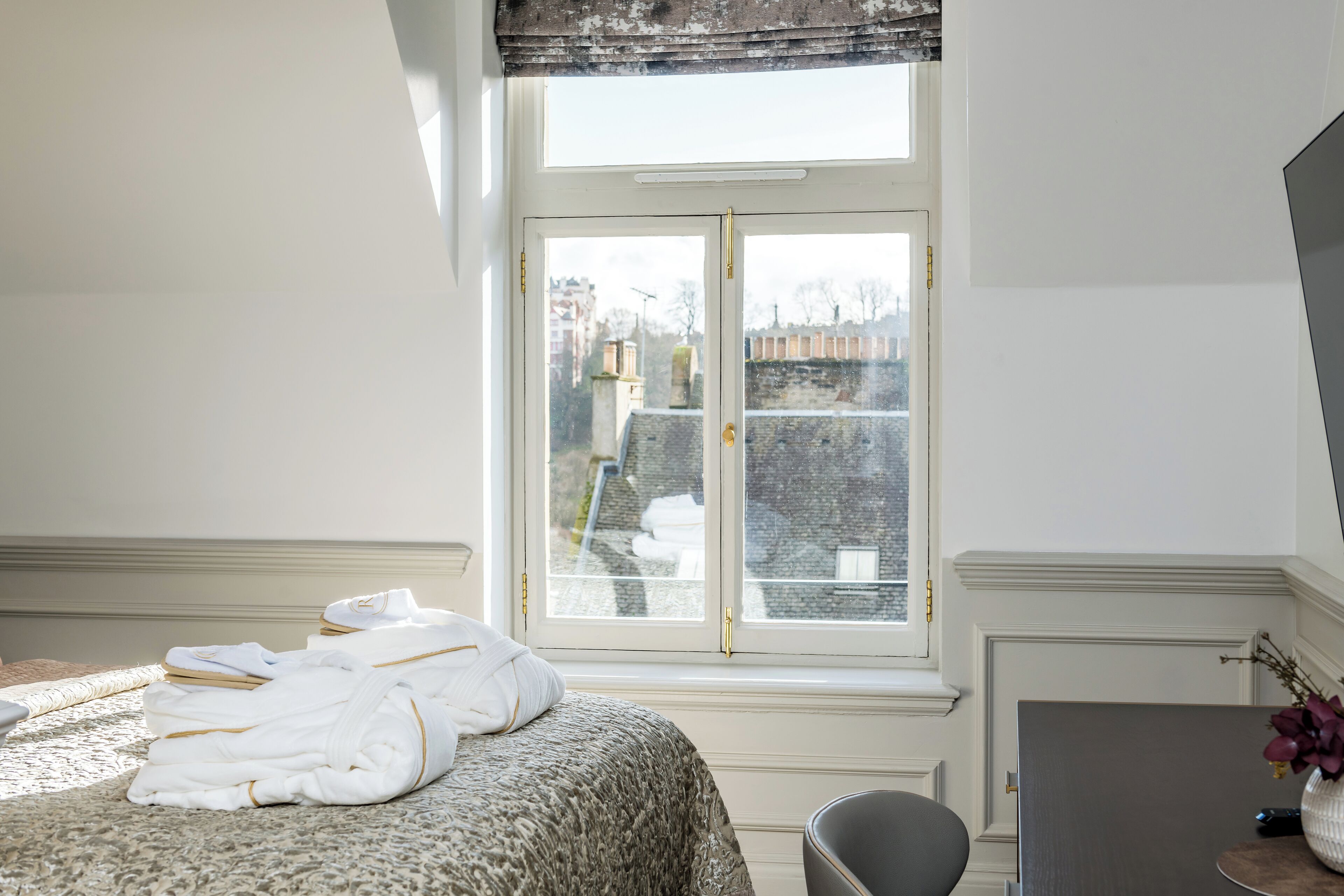 A hotel room with a bed, a desk, and a window with a view of buildings.