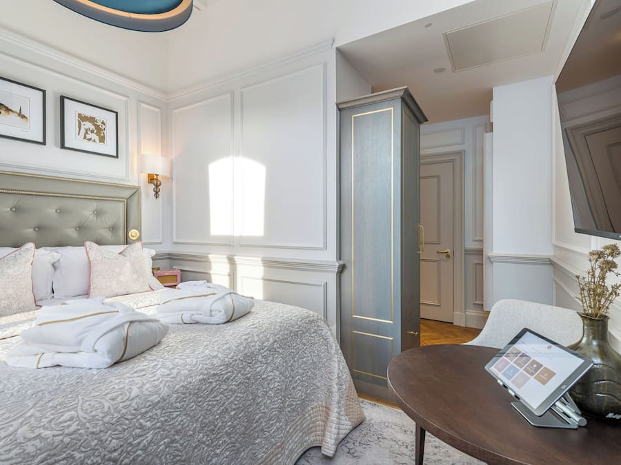 Un dormitorio ordenado con una cama grande, una mesita de noche con una tableta, y un florero con flores secas.