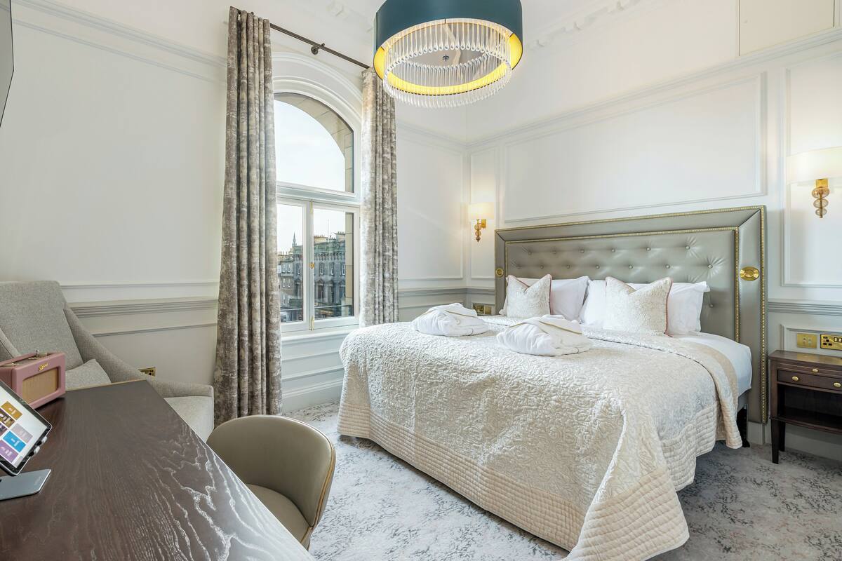 Une chambre d’hôtel avec un grand lit, un bureau avec un ordinateur portable, une chaise et une vue sur la ville par la fenêtre.