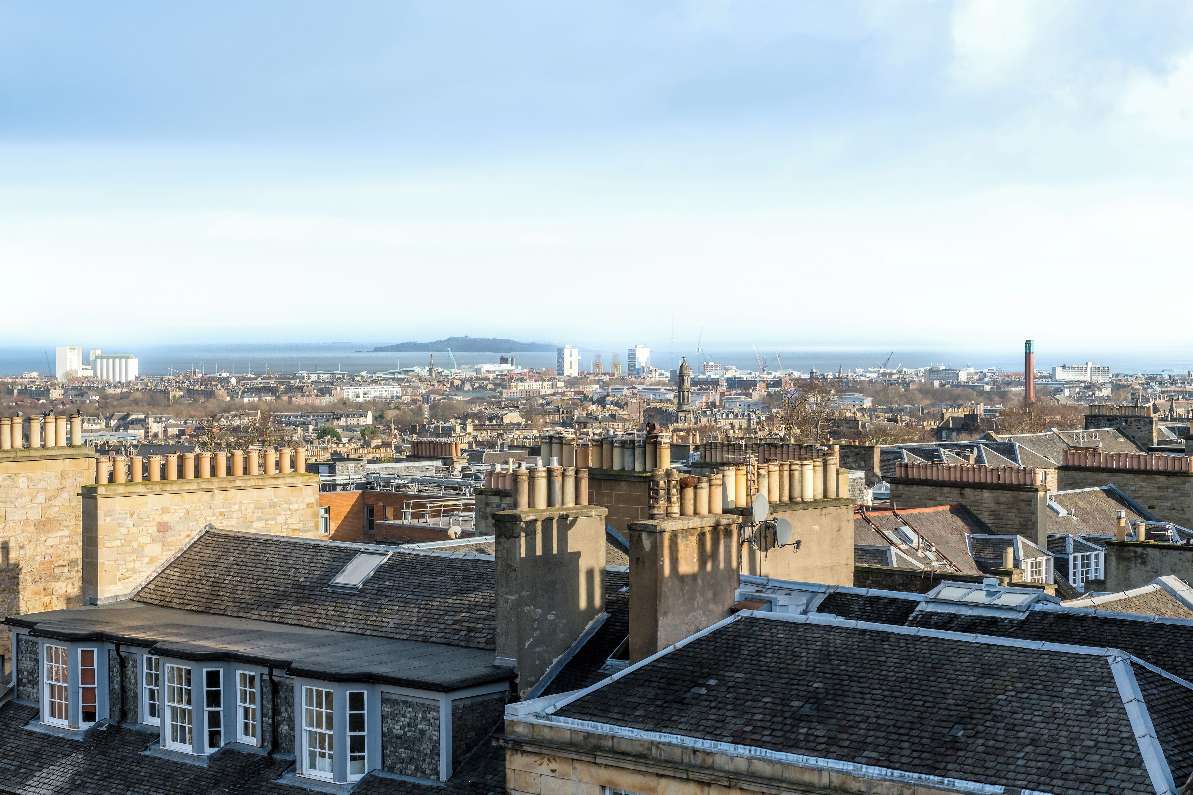 Un paysage urbain mêlant bâtiments historiques et modernes, avec une tour imposante et une vaste étendue d’eau visible au loin.