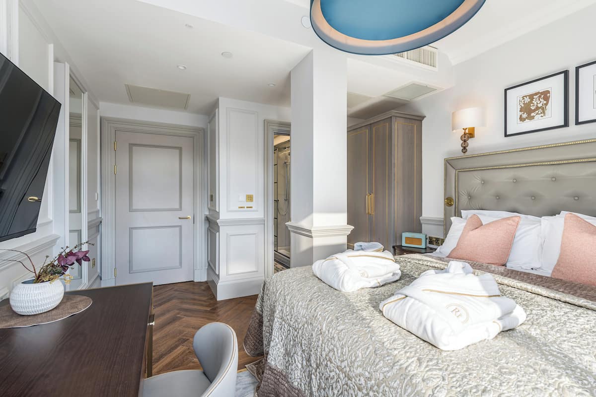 Une chambre d’hôtel avec un grand lit, une télévision, un bureau agrémenté d’un vase, et une salle de bain visible à travers une porte ouverte.