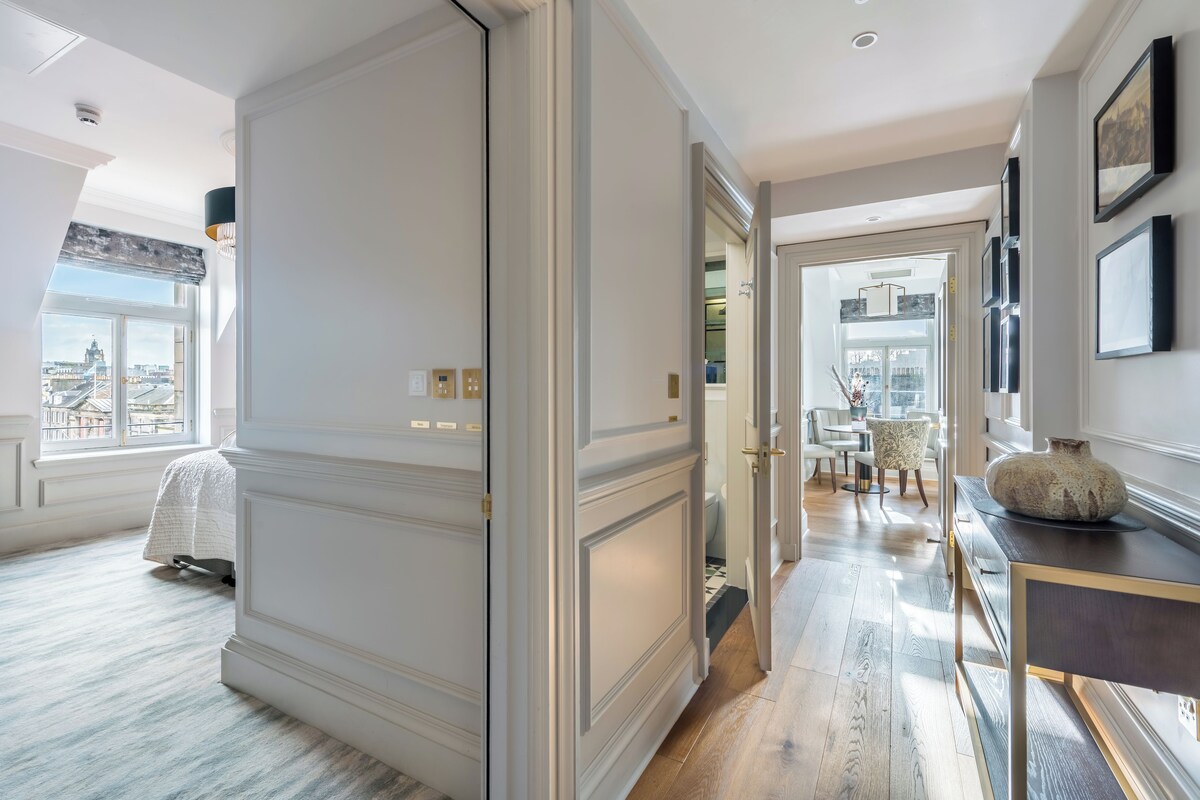 A spacious hallway with a view of the city, a dining area with chairs, and a table with a vase.