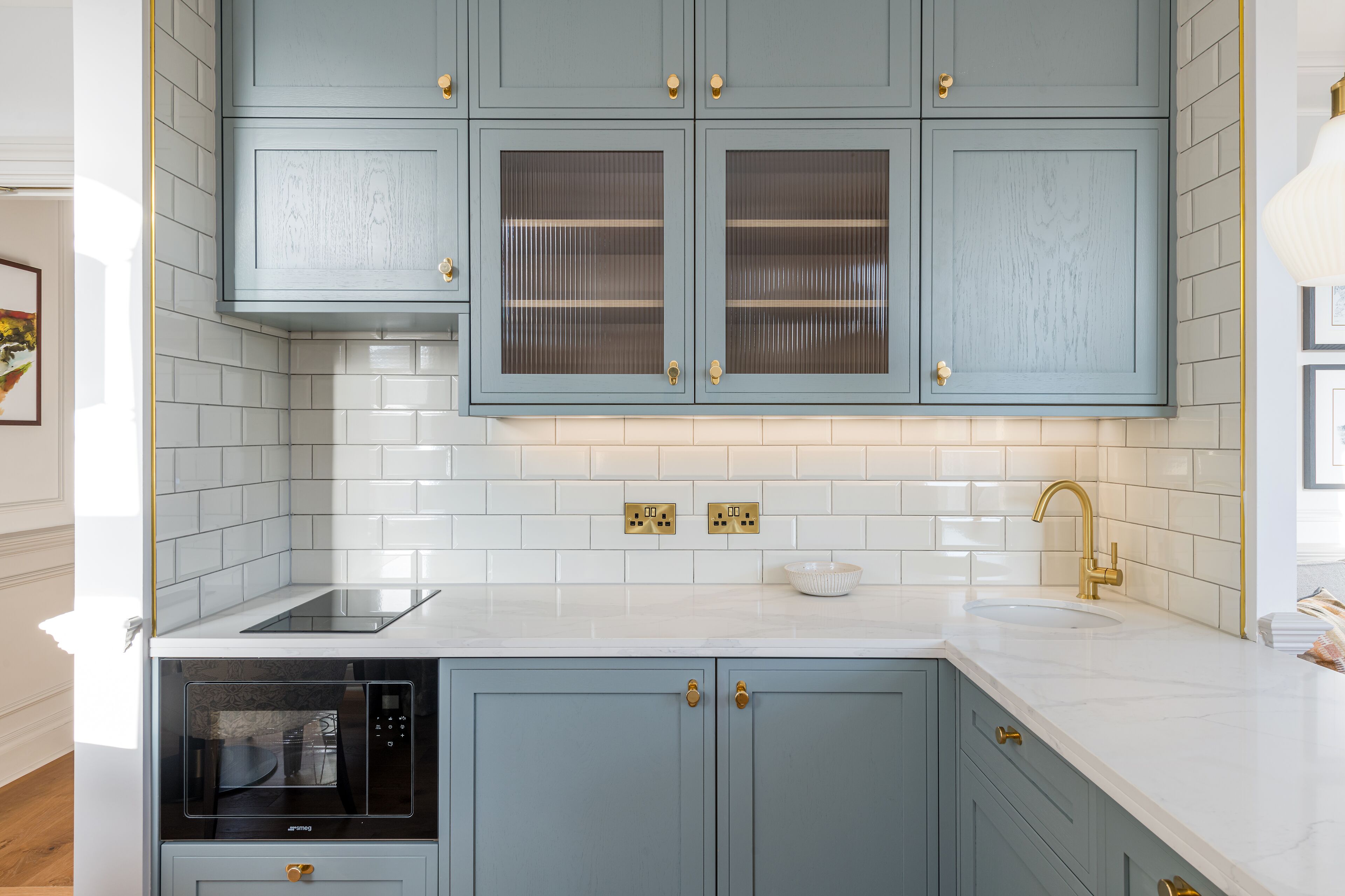 A kitchen with light blue cabinets, a white countertop, a built-in oven, and a gold faucet.
