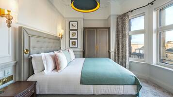 A neatly made bed with a white and teal bedspread, a wooden nightstand, and a wall-mounted lamp.